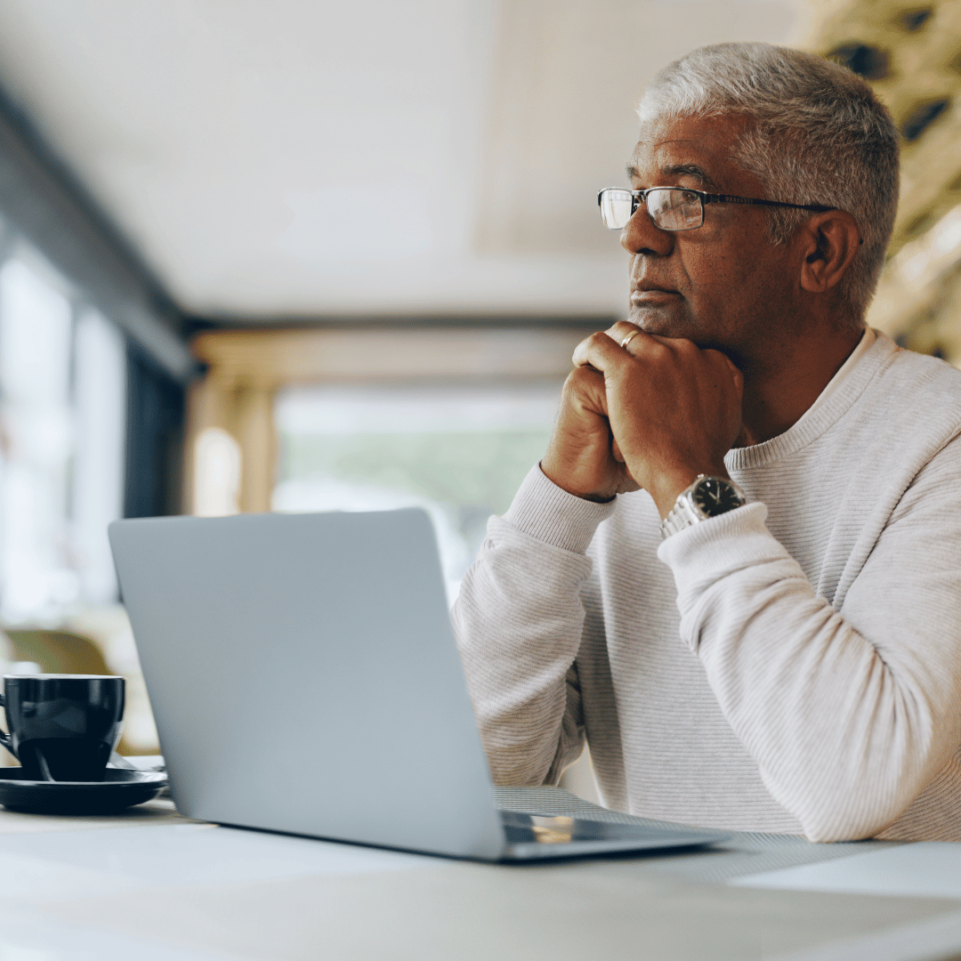 Retired man with gray hair sitting at computer, contemplating out-of-pocket health care costs and medical debt