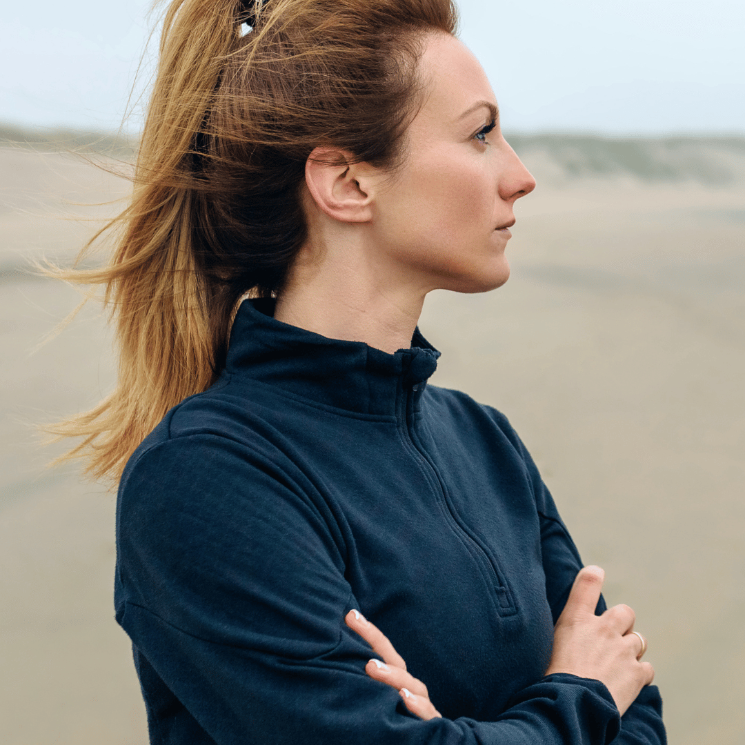 woman with arms crossed looking out across beach contemplating critical illness insurance